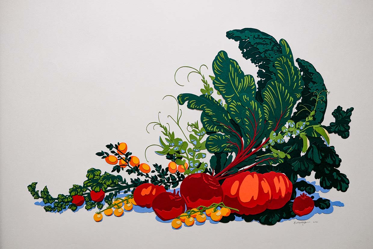 A bounty of paper produce tumbles off the page, including kale, chard, sweet peas, various tomatoes, beets, and kumquats. The greens, reds, and oranges are offset by a blue paper cast shadow.