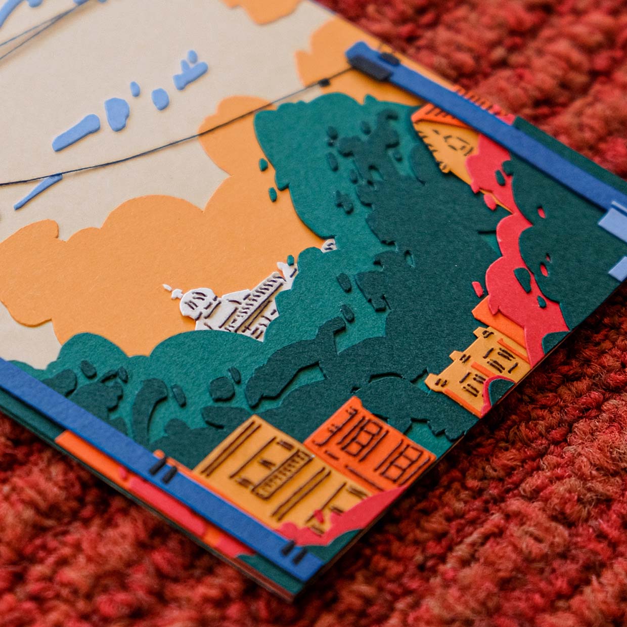 Layers of red, orange, green, and blue paper create a scene of apartment blocks against the green tree tops of Golden Gate Park. Stitched details are visible on the buildings.