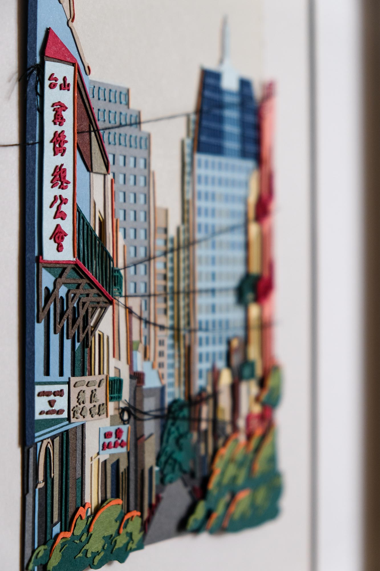 An angled view of the artwork focuses on the paper signs on the left edge, revealing the many layers of paper that make up the buildings.