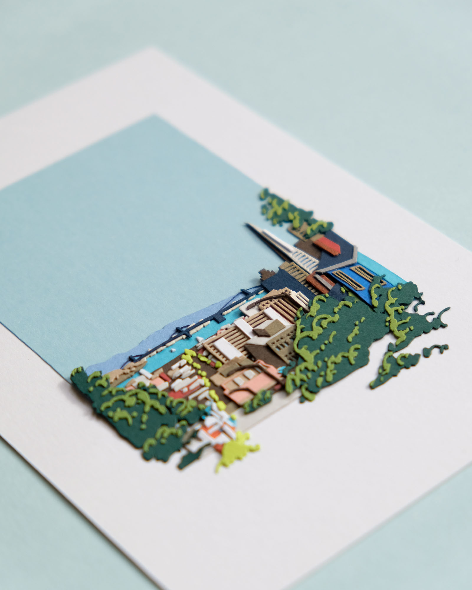 An angled view of the artwork reveals stacks of paper layers within the buildings and the foliage.