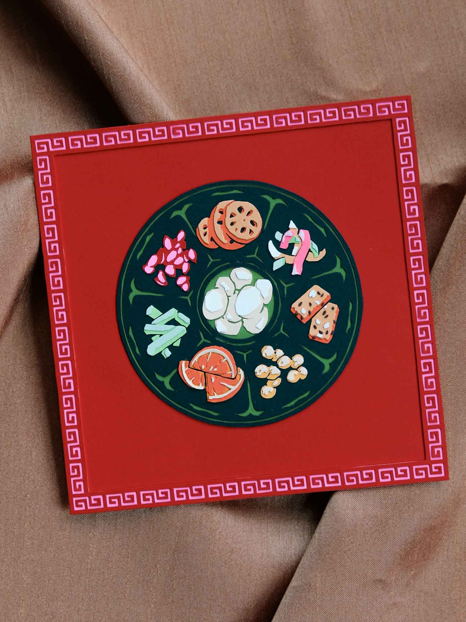 A round, deep jade green tray floats within a square of lucky red. Within the tray are eight colorful Chinese confections, including candied water chestnut, lotus, dried fruits, and seeds. The artwork rests against a shimmering copper cloth.