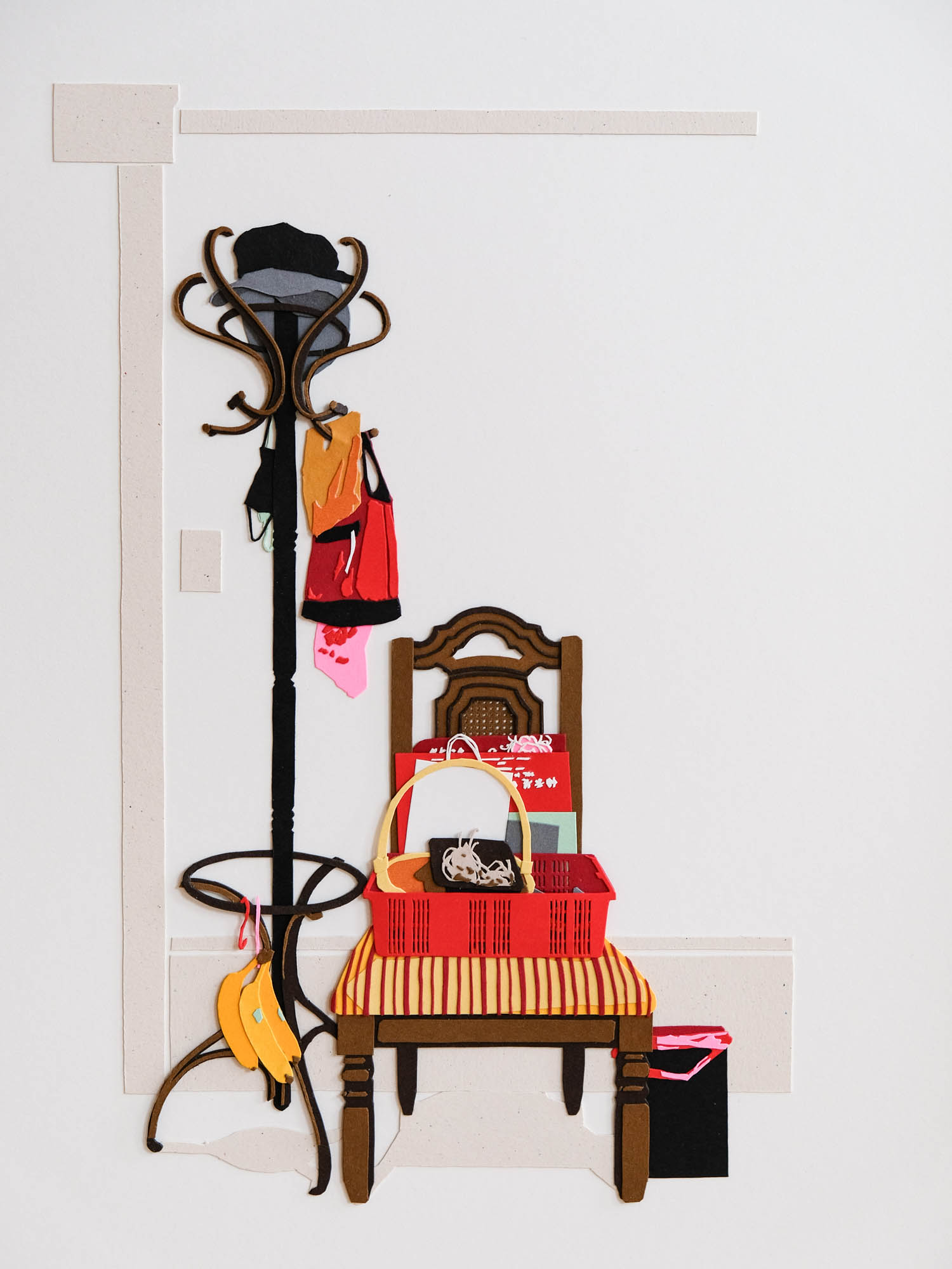 A paper coatrack stands next to a paper dining chair. Both are festooned with various bags, baskets, paper goods, and a clutch of bananas. Faint shapes hint at the architecture of the room beyond.